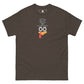 A chocolate brown t-shirt featuring a playful graphic design of a turkey face with eyes, an orange beak, and a red snood. Above the face, the text reads "TURKEY MASTER" in bold, stylized letters. The text is in the shape of a pilgrims hat. On the left sleeve, there's a rectangular logo patch, adding a unique touch. The shirt is laid out flat, showcasing the entire design clearly.