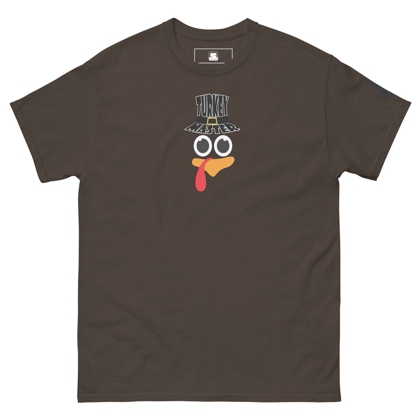 A chocolate brown t-shirt featuring a playful graphic design of a turkey face with eyes, an orange beak, and a red snood. Above the face, the text reads "TURKEY MASTER" in bold, stylized letters. The text is in the shape of a pilgrims hat. On the left sleeve, there's a rectangular logo patch, adding a unique touch. The shirt is laid out flat, showcasing the entire design clearly.