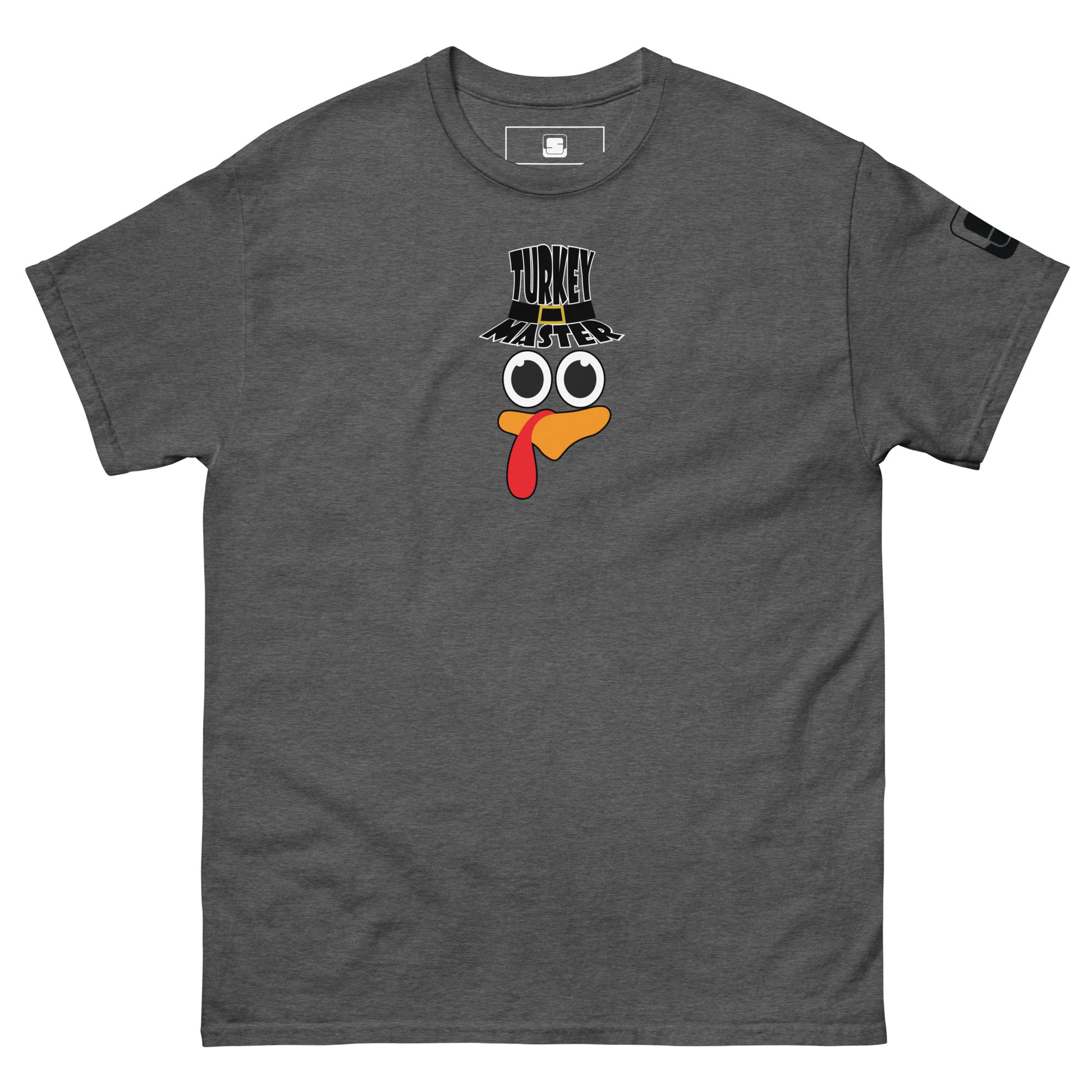 A dark heather t-shirt featuring a playful graphic design of a turkey face with eyes, an orange beak, and a red snood. Above the face, the text reads "TURKEY MASTER" in bold, stylized letters. The text is in the shape of a pilgrims hat. On the left sleeve, there's a rectangular logo patch, adding a unique touch. The shirt is laid out flat, showcasing the entire design clearly.