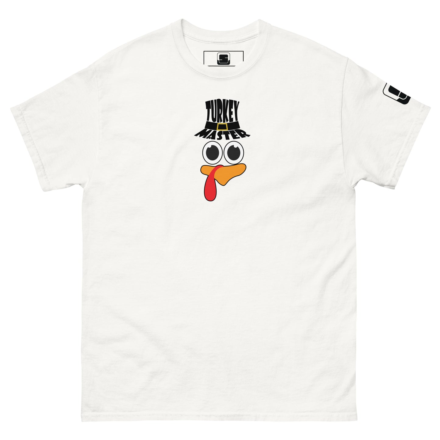 A white t-shirt featuring a playful graphic design of a turkey face with eyes, an orange beak, and a red snood. Above the face, the text reads "TURKEY MASTER" in bold, stylized letters. The text is in the shape of a pilgrims hat. On the left sleeve, there's a rectangular logo patch, adding a unique touch. The shirt is laid out flat, showcasing the entire design clearly.