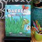 An outdoor display featuring the coloring book 'DARREN The Dirty Dino' on a black easel. The cover shows a cheerful green dinosaur peeking through tall green grass, with a friendly butterfly hovering overhead. Next to the easel is a green mug filled with colorful crayons, set against a backdrop of lush plants and a lattice design.