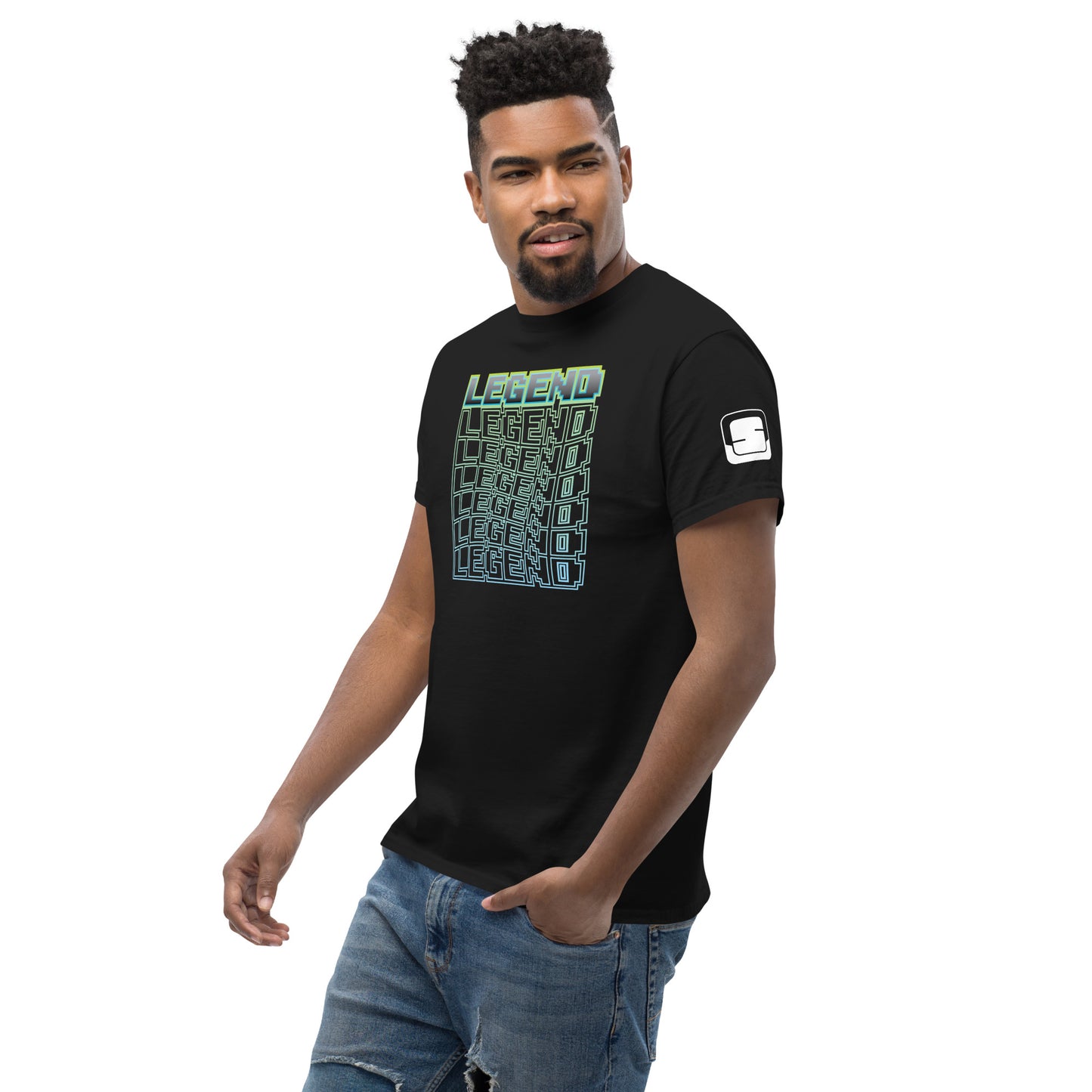 Confident man with a slight smile wearing a black t-shirt featuring a vibrant 'LEGEND' graphic in a green-to-blue gradient cube illusion, with a logo patch on the sleeve, paired with blue jeans, against a white background.