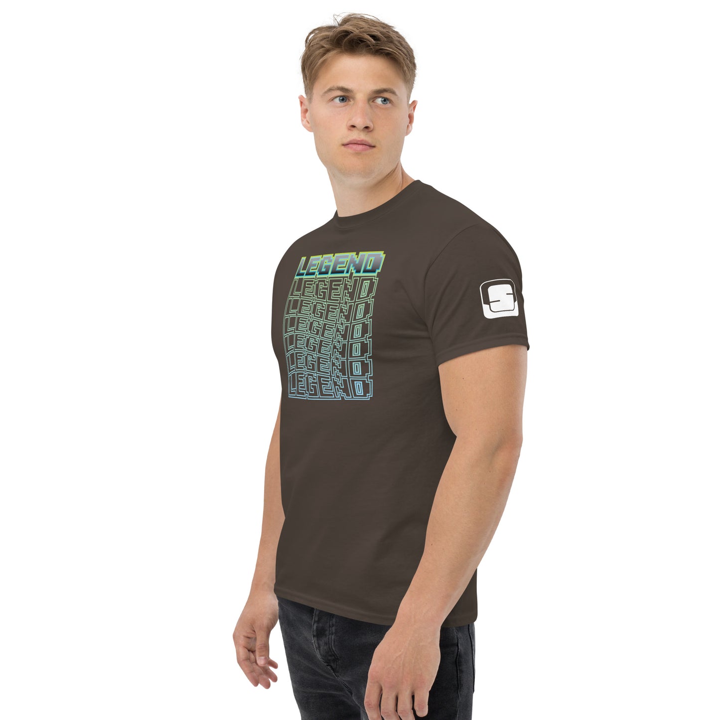 A man with a neutral expression wearing a dark brown t-shirt with a stylized graphic that reads 'LEGEND' repeatedly in a green-to-blue gradient, creating a 3D cube effect, with a logo patch on the sleeve, standing against a white background.