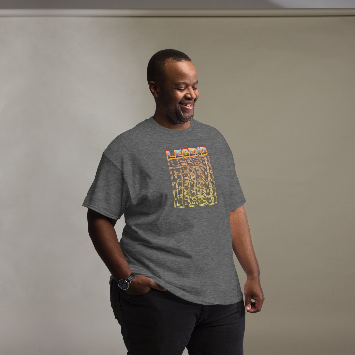 Man smiling and standing casually in a grey t-shirt featuring a pixel-style 'LEGEND' text in an orange to yellow gradient with a digital cube illusion, complemented by a simple grey background.