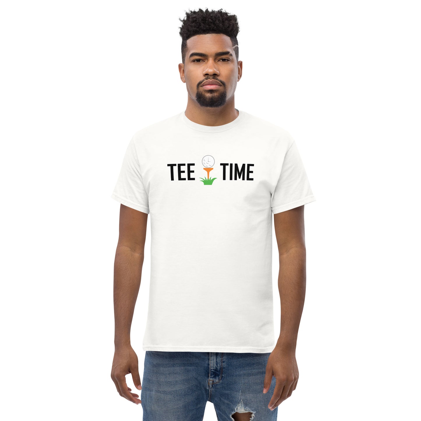 The image shows a man facing forward wearing a plain white t-shirt with a graphic and text. The graphic is centered on the chest area and depicts a golf tee with a golf ball on top; growing from the tee is a small green plant. Above the graphic, the text reads "TEE TIME" in black capital letters. The man has short curly hair, a neatly trimmed beard, and a neutral expression. He is wearing blue jeans and the background is plain white, focusing all attention on the t-shirt design. 