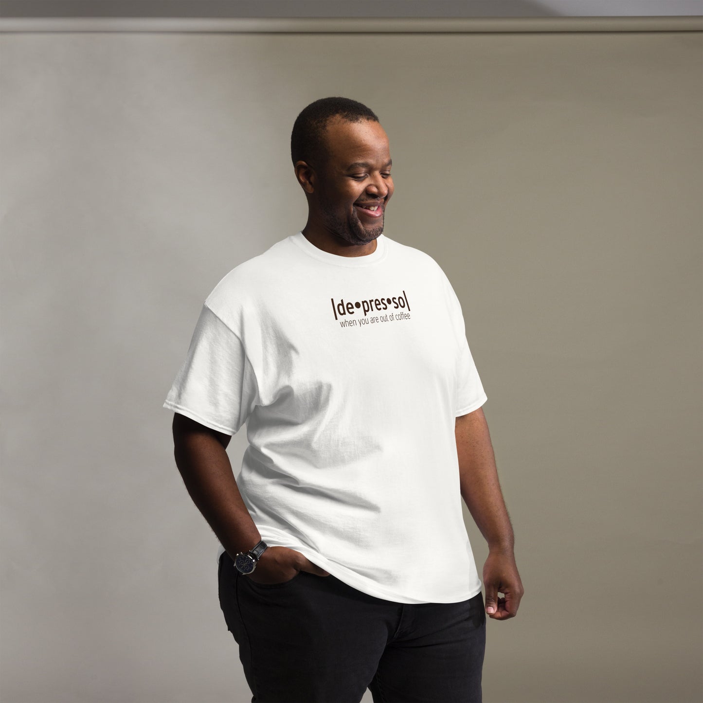 Man chuckling to himself, clad in a casual white t-shirt with the quirky statement 'depresso' and 'when you are out of coffee' in a straightforward font, paired with black pants and a watch, in a room with a gradient grey background.