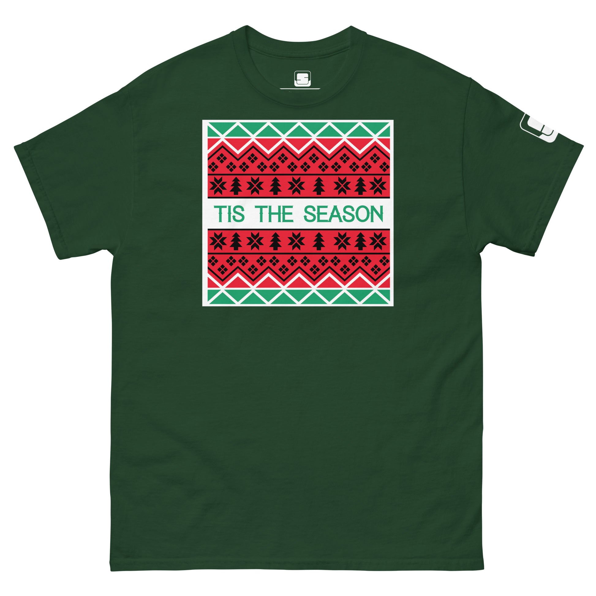A dark green t-shirt featuring a holiday-themed design similar to a Christmas sweater. The central rectangle contains patterns of stars, geometric shapes, and traditional motifs in red, white, and black. The phrase 'TIS THE SEASON' is prominently displayed in bold, green letters on a white background, adding a festive touch to the shirt.