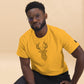 A young African American man wearing glasses models a vibrant yellow T-shirt featuring a detailed, geometric deer head design in black. He poses with a thoughtful expression, seated against a soft beige background, adding a stylish and contemporary touch to the casual look.