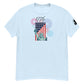 A light blue t-shirt featuring a festive Fourth of July design. The central graphic combines the Statue of Liberty and an American flag, with the year '1776' emblazoned above in a decorative script. The background is filled with vibrant fireworks in red, blue, and purple, symbolizing American independence and celebration.