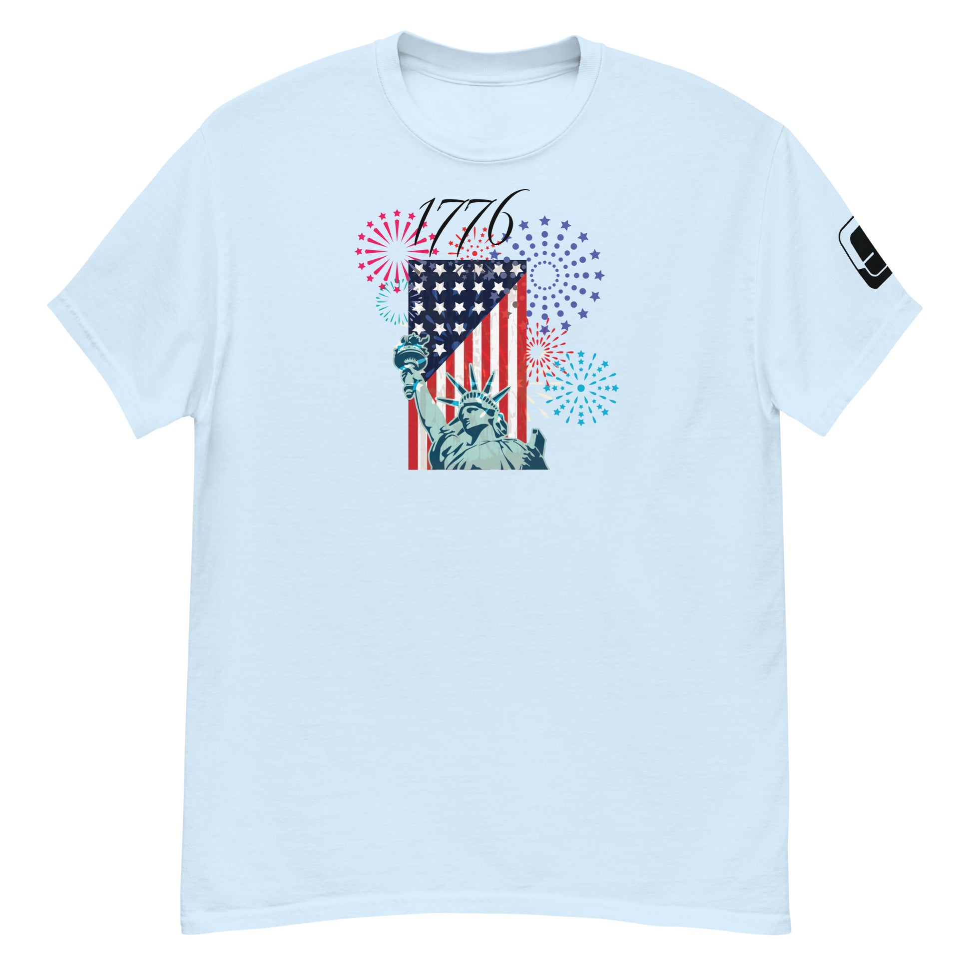 A light blue t-shirt featuring a festive Fourth of July design. The central graphic combines the Statue of Liberty and an American flag, with the year '1776' emblazoned above in a decorative script. The background is filled with vibrant fireworks in red, blue, and purple, symbolizing American independence and celebration.