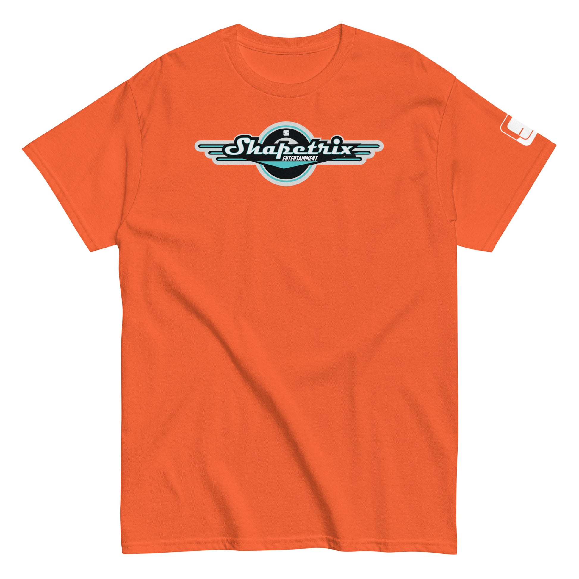 A plain orange-colored t-shirt laid flat, featuring the Shapetrix Entertainment logo centrally placed. The logo includes the brand name in stylish teal and white lettering inside a black circle, accented by elongated white wing-like graphics on both sides. A tag on the left sleeve shows a tiny black and white Shapetrix Entertainment label, adding a sophisticated touch to the vibrant shirt.