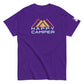 A vibrant purple t-shirt featuring the  a colorful mountain motif with three overlaid peaks in muted shades of yellow and orange, and the phrase "HAPPY CAMPER" beneath in a bold, pale blue sans-serif font. The t-shirt has a casual, crew neck style with a sleeve tag, presented on a plain white background to emphasize the design's details.