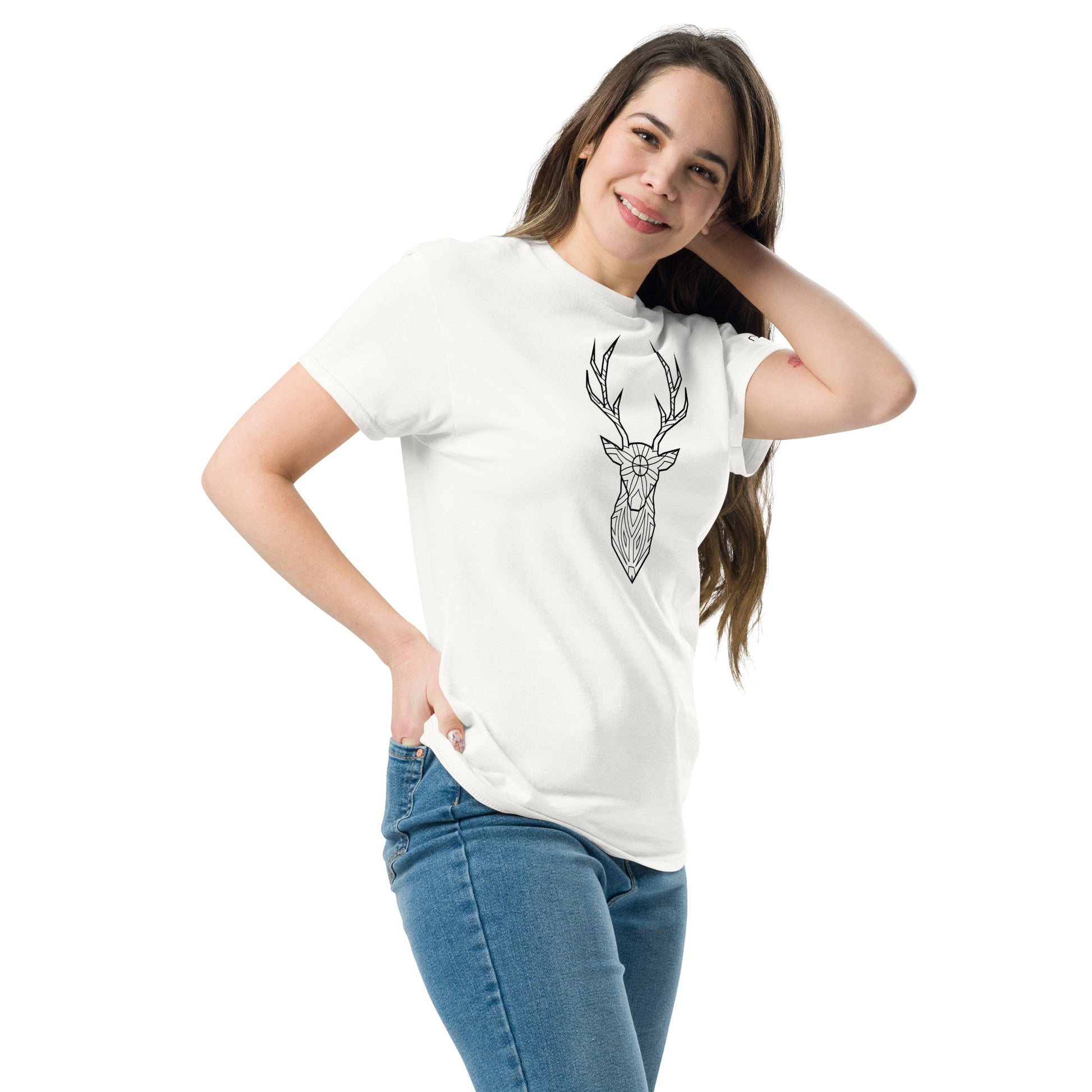 A young Caucasian woman with long brown hair smiles gently while posing in a white T-shirt featuring a black geometric deer head design. She stands with one hand on her hip and the other touching her hair, wearing blue jeans, against a plain white background, giving off a casual yet stylish vibe.