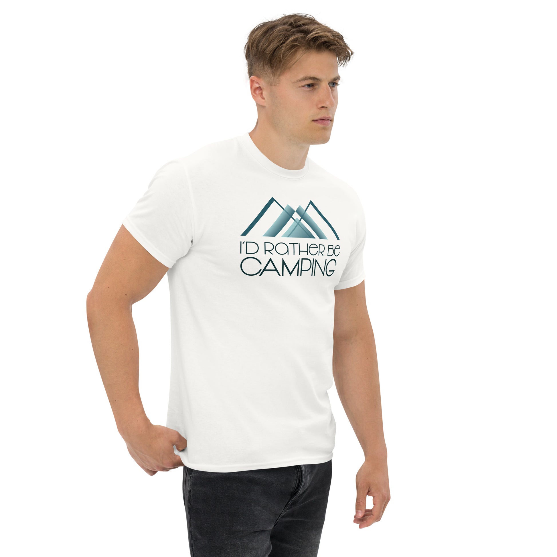 A young man stands wearing a white t-shirt featuring the design "I'D RATHER BE CAMPING" with a graphic of a stylized blue and white mountain above the text. He is looking slightly to the side, with a neutral expression, against a plain white background. His casual pose, with one hand partially in his dark jeans pocket, complements the laid-back outdoor theme of the shirt.