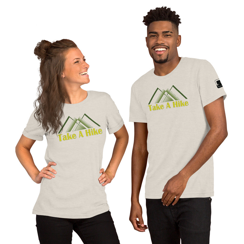 A cheerful Caucasian woman and a smiling African American man stand together, each wearing a light gray t-shirt with the phrase "Take A Hike" in yellow text, beneath a green mountain design. The woman, with her long hair styled in a half-updo, looks to her left, while the man, featuring a well-kept beard and stylish haircut, looks at the camera. They are set against a neutral background that highlights their vibrant expressions and matching t-shirts.