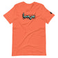 Heather orange t-shirt featuring central turquoise Arabic calligraphy with black shadow and scattered ink dots, accompanied by a small black logo patch on the sleeve, displayed against a white background.