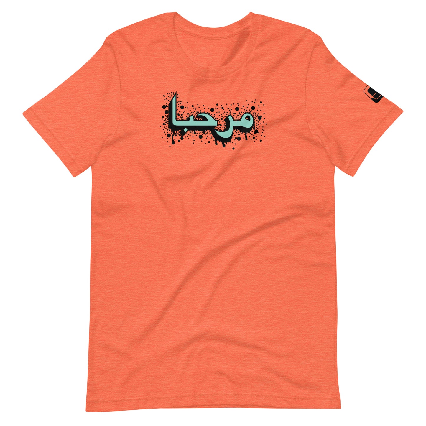 Heather orange t-shirt featuring central turquoise Arabic calligraphy with black shadow and scattered ink dots, accompanied by a small black logo patch on the sleeve, displayed against a white background.
