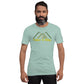A confident middle-aged man with a neatly groomed beard and short hair stands wearing a soft mint green t-shirt that features a design of stylized green mountains topped by the phrase "Take A Hike" in yellow text. His serious expression and direct gaze at the camera convey a strong presence. He sports a black watch on his left wrist, which complements his casual yet refined style. The t-shirt fits him comfortably, accentuating a relaxed outdoor enthusiast vibe against a plain background.