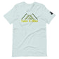 A light gray t-shirt featuring a stylized design of green mountains above the phrase "Take A Hike" in bold, yellow text. The graphic design includes three overlapping mountain peaks created with clean lines and geometric shapes. The t-shirt has a relaxed fit with a crew neck and short sleeves, and a small black logo patch is visible on the right sleeve. It is laid out flat against a white background, highlighting the simple and outdoorsy theme of the shirt.