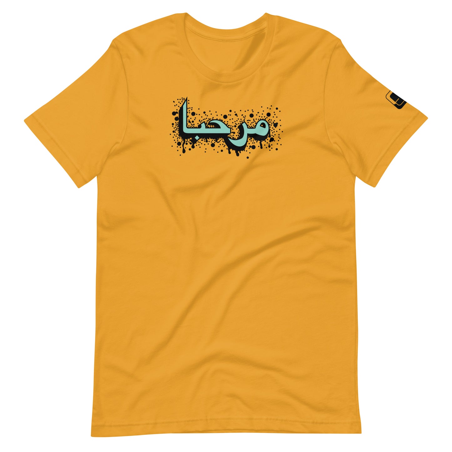 Mustard yellow t-shirt featuring central turquoise Arabic calligraphy with black shadow and scattered ink dots, accompanied by a small black logo patch on the sleeve, displayed against a white background.