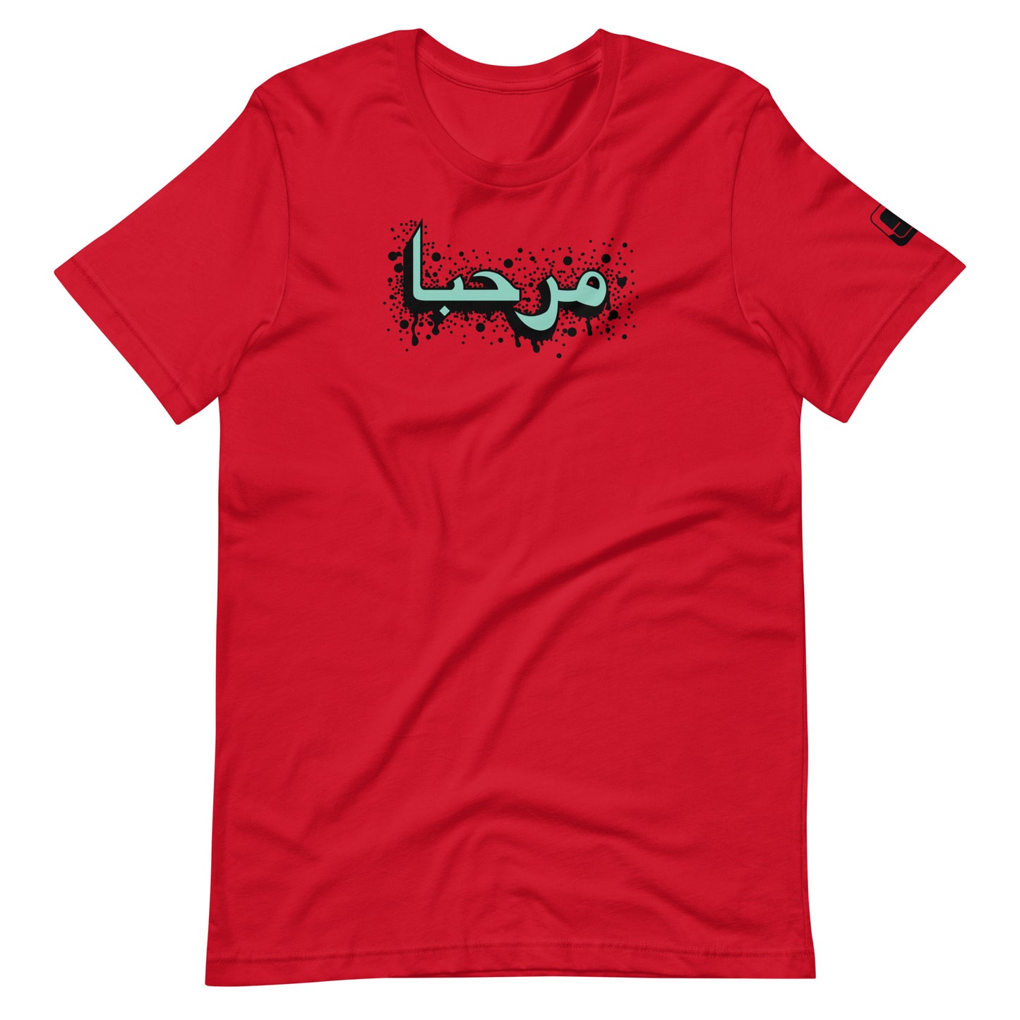 Red t-shirt featuring central turquoise Arabic calligraphy with black shadow and scattered ink dots, accompanied by a small black logo patch on the sleeve, displayed against a white background.
