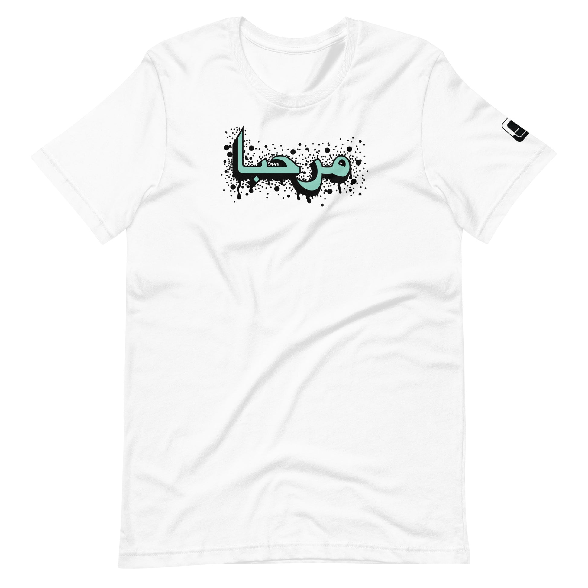 White t-shirt featuring central turquoise Arabic calligraphy with black shadow and scattered ink dots, accompanied by a small black logo patch on the sleeve, displayed against a white background.