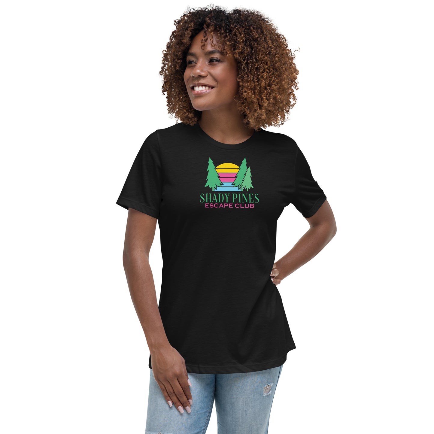 A cheerful woman models a black t-shirt featuring the "Shady Pines Escape Club" logo. The design showcases two green pine trees flanking a vibrant sunset with horizontal stripes in yellow, pink, and purple. Beneath the sunset, "SHADY PINES" is displayed in bold green text, with "ESCAPE CLUB" in smaller pink lettering below. The lively design adds a playful touch, making the t-shirt ideal for casual and outdoor-inspired looks.