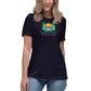 A woman wearing a dark navy blue t-shirt featuring a colorful graphic design with two green pine trees framing a vibrant sunset of pink, orange, and yellow stripes. Below the image, the text reads "Shady Pines Escape Club" in green and pink letters. The shirt pairs with casual blue jeans for a relaxed look.