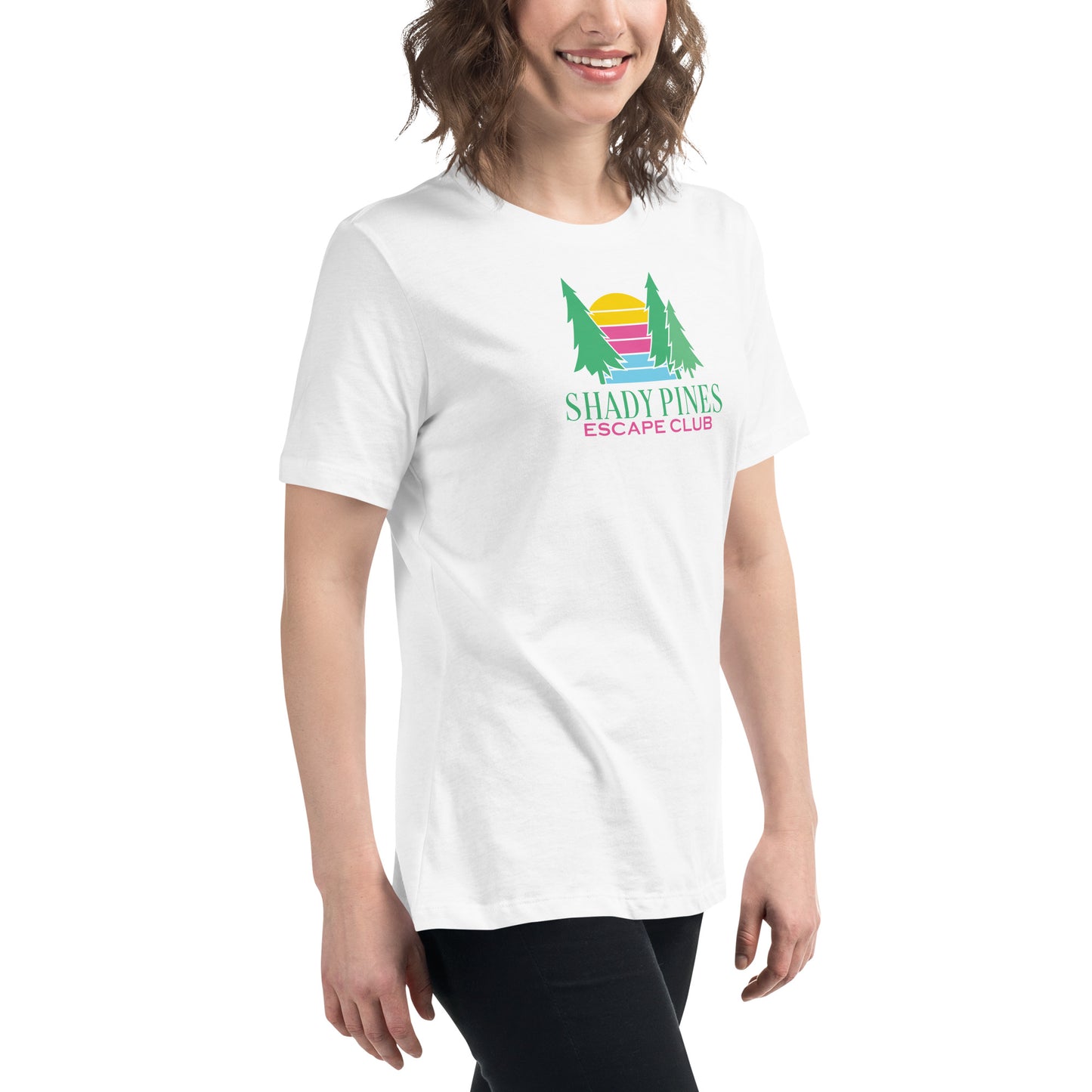 A joyful woman models a white t-shirt featuring the "Shady Pines Escape Club" logo. The logo depicts two green pine trees on either side of a stylized sunset with horizontal stripes in yellow, pink, purple, and blue. Below the sunset, "SHADY PINES" is written in bold, green text, while "ESCAPE CLUB" is detailed below in smaller pink letters. The simple yet colorful design of the t-shirt is both eye-catching and playful, perfect for casual wear.